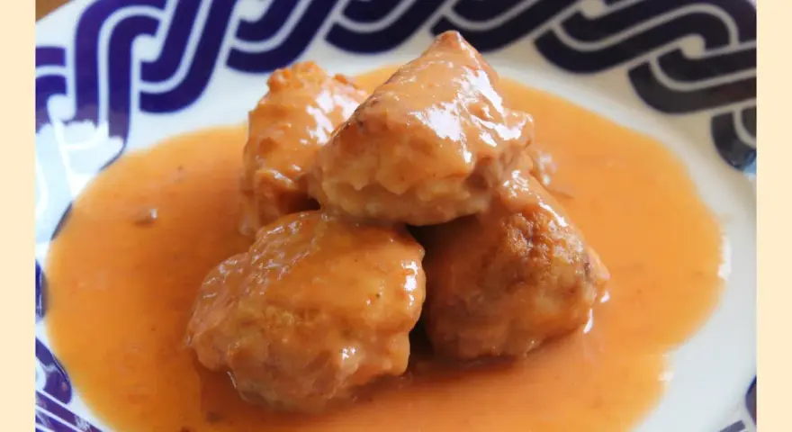 Deliciosas albóndigas de rape en una cremosa salsa naranja, servidas en un plato con borde azul.
