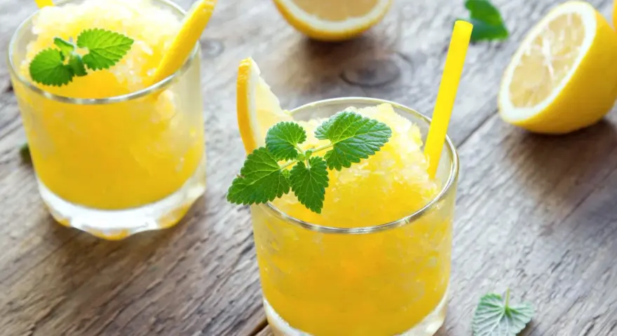 Refrescante granizado de limón, perfecto para un día caluroso. Servido en vasos con rodajas de limón y hojas de menta.