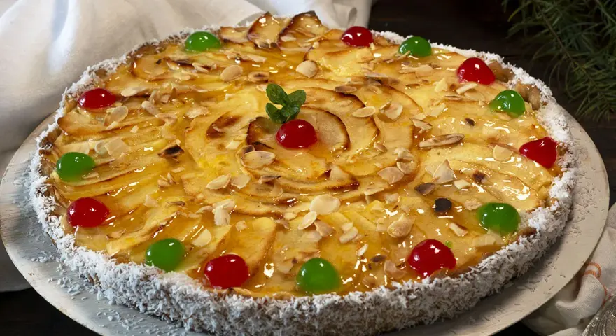 Deliciosa tarta de manzana cubierta de almendras laminadas y cerezas rojas y verdes. El borde está cubierto de coco rallado.