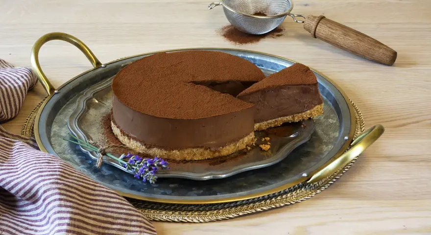 Delicioso pastel de chocolate cubierto de cacao, con una rebanada servida en una bandeja de plata, decorado con lavanda.