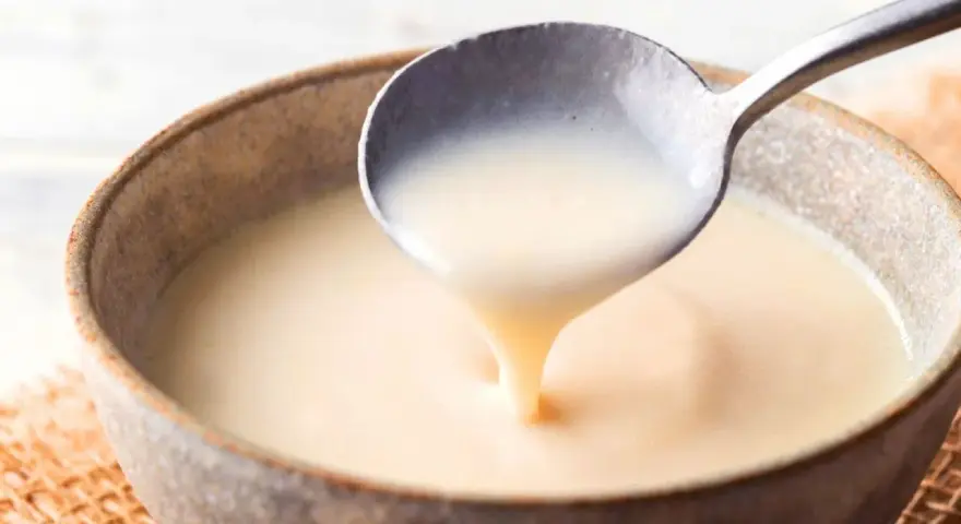 Cuchara sirviendo crema inglesa cremosa en un cuenco rústico.