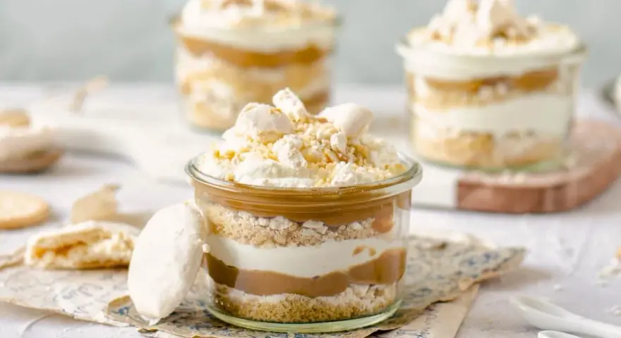Postres en vaso con capas de bizcocho, crema y dulce de leche, coronados con merengue y polvito canario.