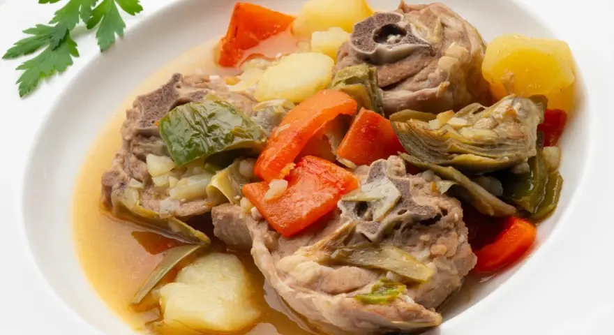 Cordero guisado receta tradicional con patatas, zanahorias y alcachofas en un plato blanco.