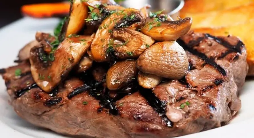 Solomillo de ternera guisado con champiñones salteados y perejil picado, servido en un plato blanco.