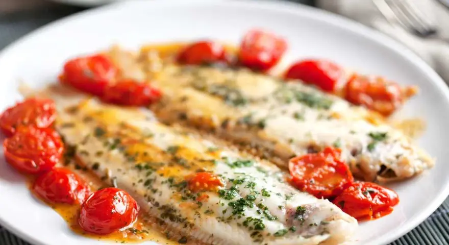 Dos filetes de lenguado a la plancha, servidos con tomates cherry salteados y perejil picado.