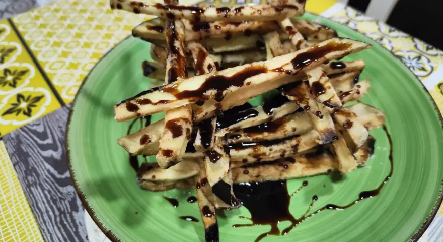 Berenjenas fritas en forma de bastones, bañadas en miel oscura, servidas en un plato verde.
