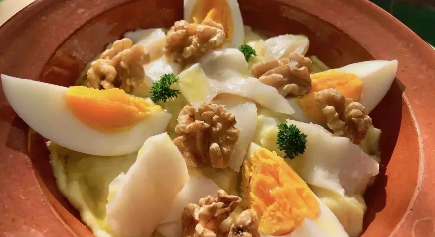 Delicioso plato de atascaburras receta con huevo duro, nueces y perejil en una cazuela de barro.
