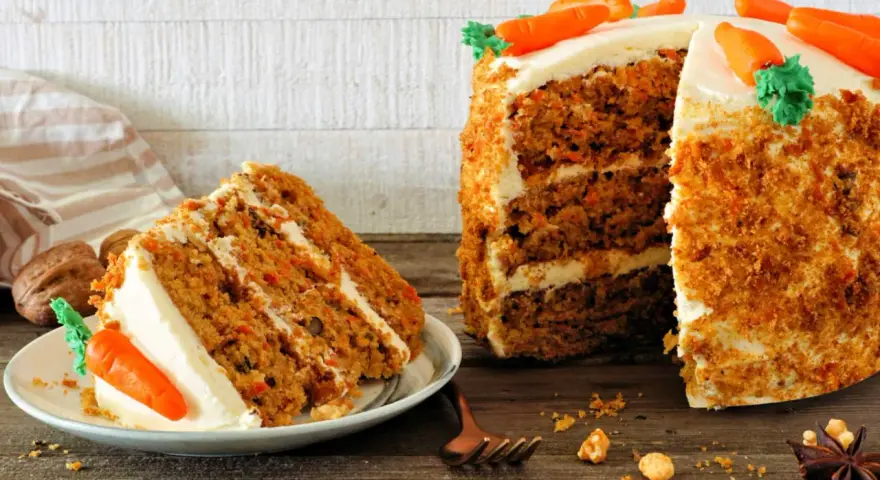 Deliciosa tarta de zanahoria con glaseado cremoso y decoraciones de zanahorias. Una rebanada ya servida en un plato.