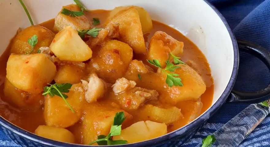 Un reconfortante plato de patatas con bacalao en una salsa rojiza, adornado con perejil fresco.