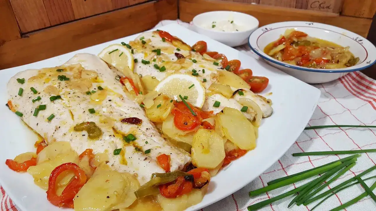 Deliciosa merluza al horno con patatas, pimientos y tomates cherry. Un plato principal perfecto para cualquier ocasión.