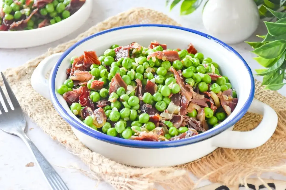 Un plato de guisantes con jamón, un clásico español, servido en una cazuela blanca con borde azul.
