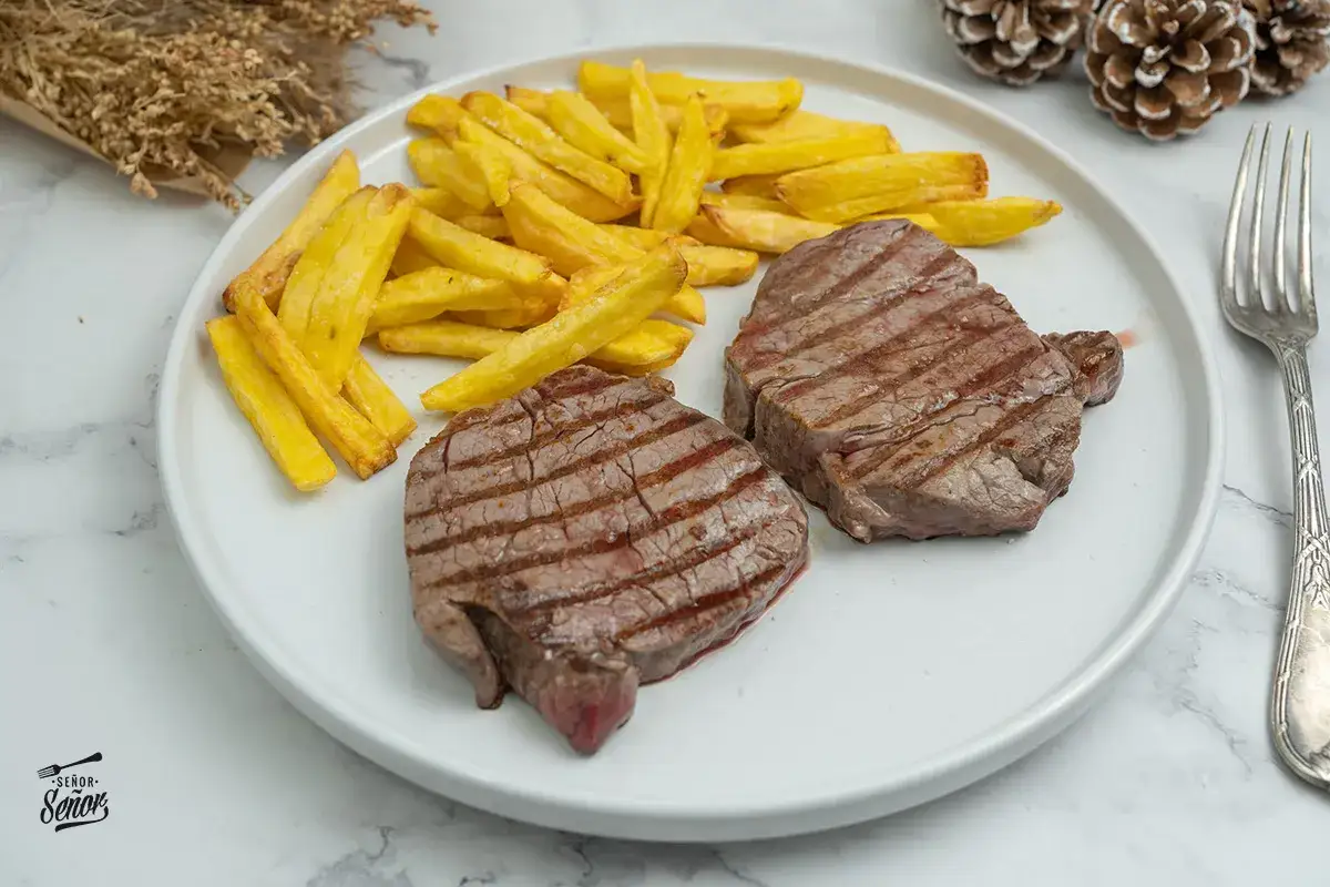 Dos jugosos solomillos de ternera a la plancha con patatas fritas doradas.