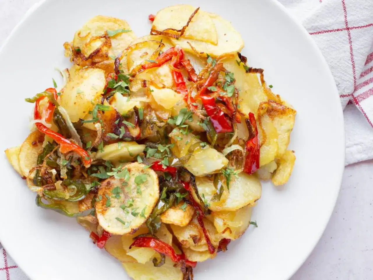 Patatas a lo pobre, un plato casero con patatas fritas, pimientos rojos y verdes, y cebolla, todo espolvoreado con perejil fresco.