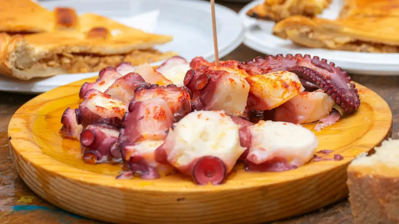 Pulpo cocido en rodajas, sazonado con pimentón y servido en plato de madera.