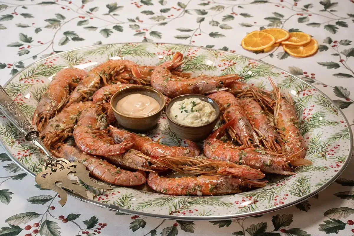 Gambones al horno servidos en una bandeja festiva con dos salsas y rodajas de naranja.