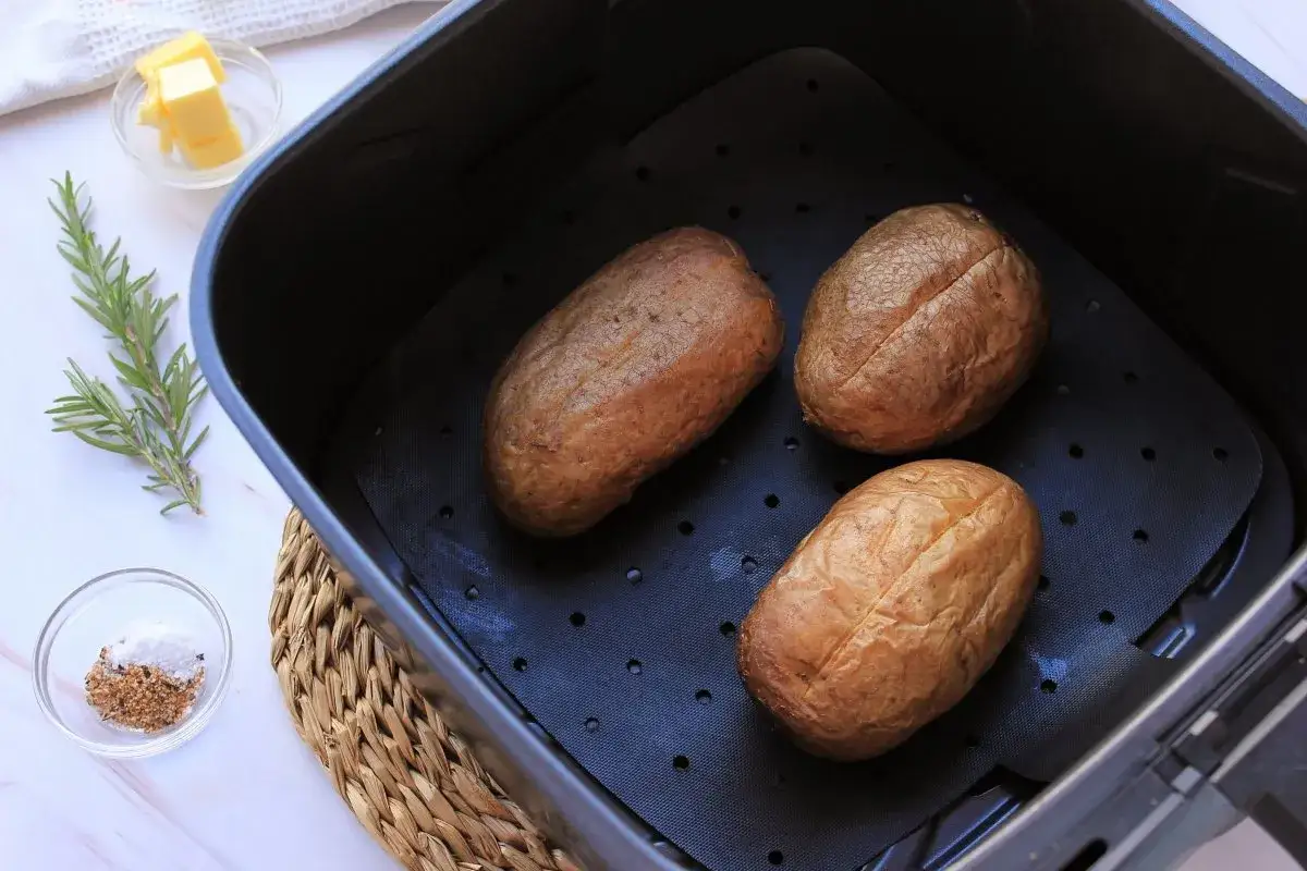 Tres patatas asadas en freidora de aire, listas para sazonar con sal, pimienta y romero.