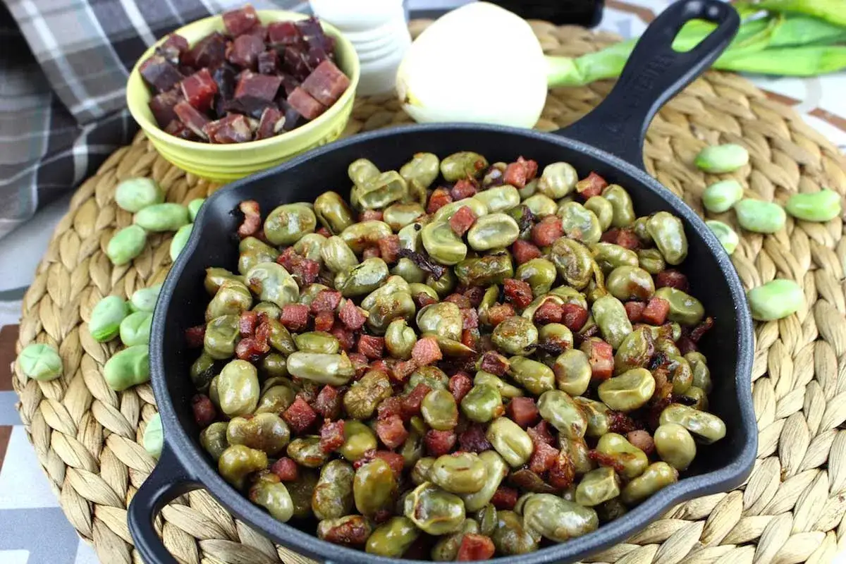 Habas tiernas salteadas con trocitos de jamón crujiente en una sartén de hierro fundido. Un plato sencillo y delicioso.