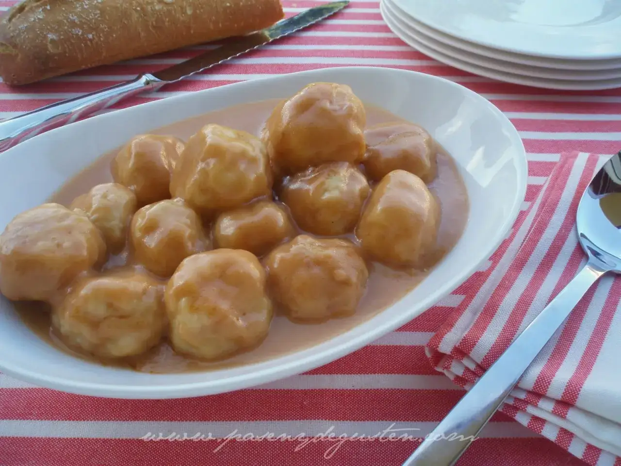 Albondigas de rape en una salsa cremosa, servidas en un plato blanco sobre un mantel a rayas rojas y blancas.