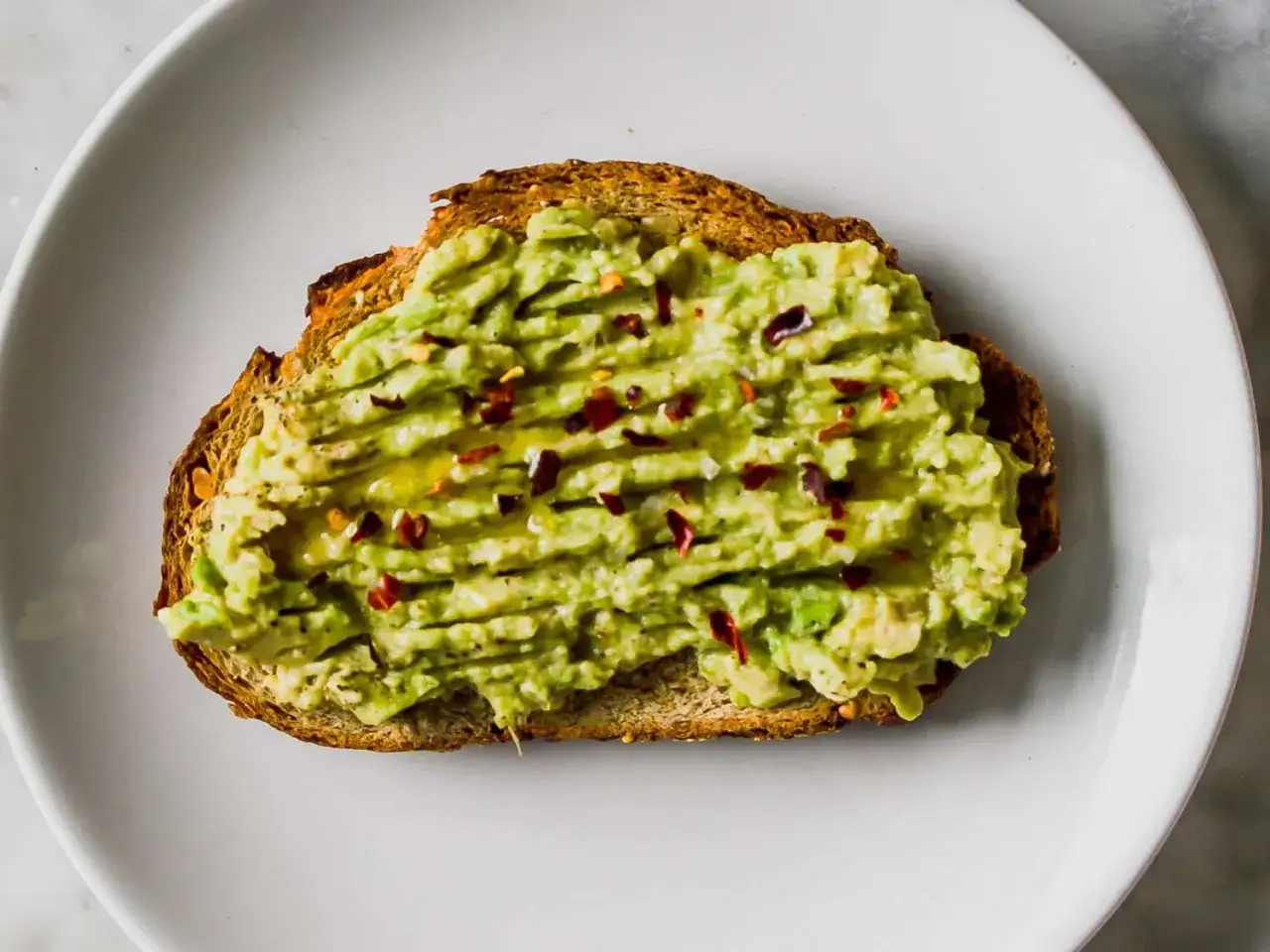 Tostada de pan integral con aguacate machacado, aceite de oliva y hojuelas de chile rojo. Una de las muchas recetas con aguacate.