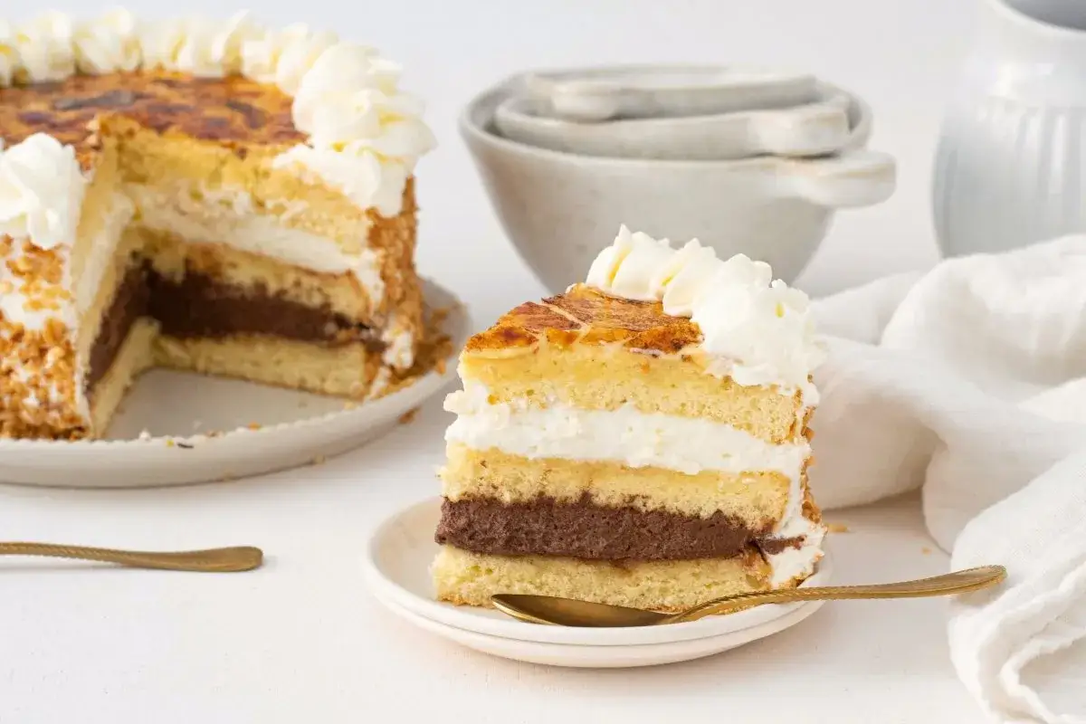 Una rebanada de tarta San Marcos con capas de bizcocho, crema y chocolate, coronada con nata y caramelo tostado.