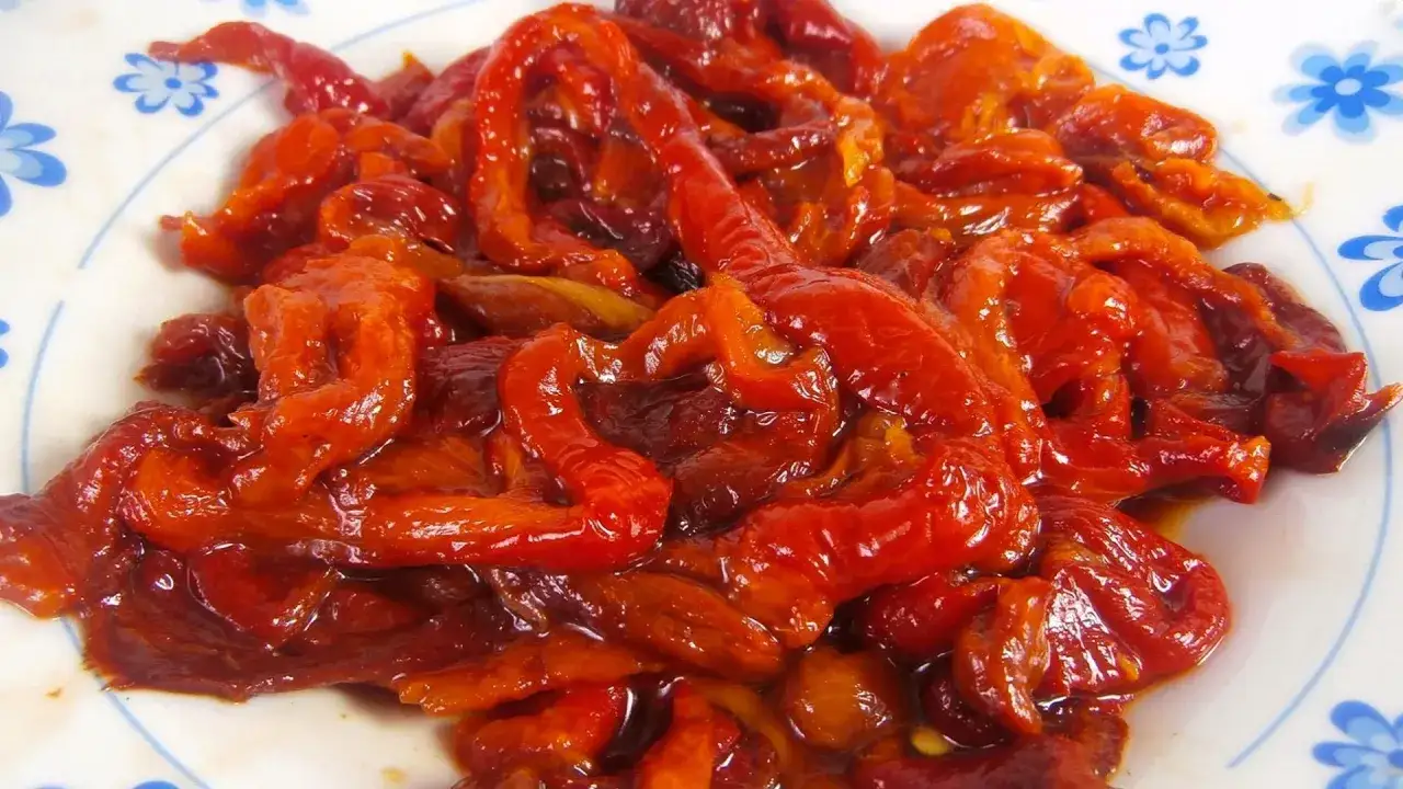 Pimientos asados, tiernos y jugosos, con un brillo apetitoso, servidos en un plato blanco con un borde azul.