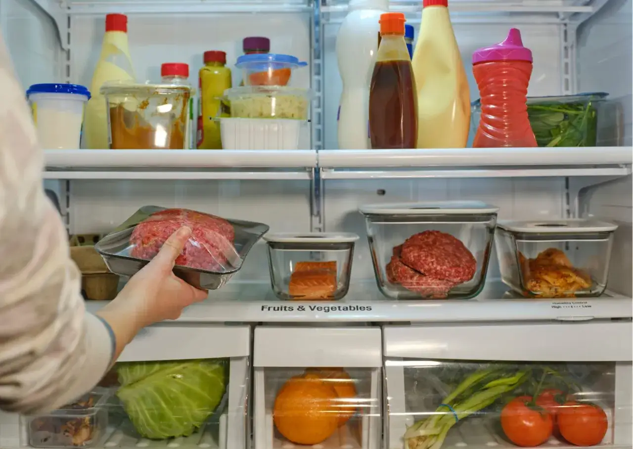 Persona guarda carne picada en su envase. ¿Cuánto dura la carne en la nevera? Hay salmón, hamburguesas y pollo cocinado.