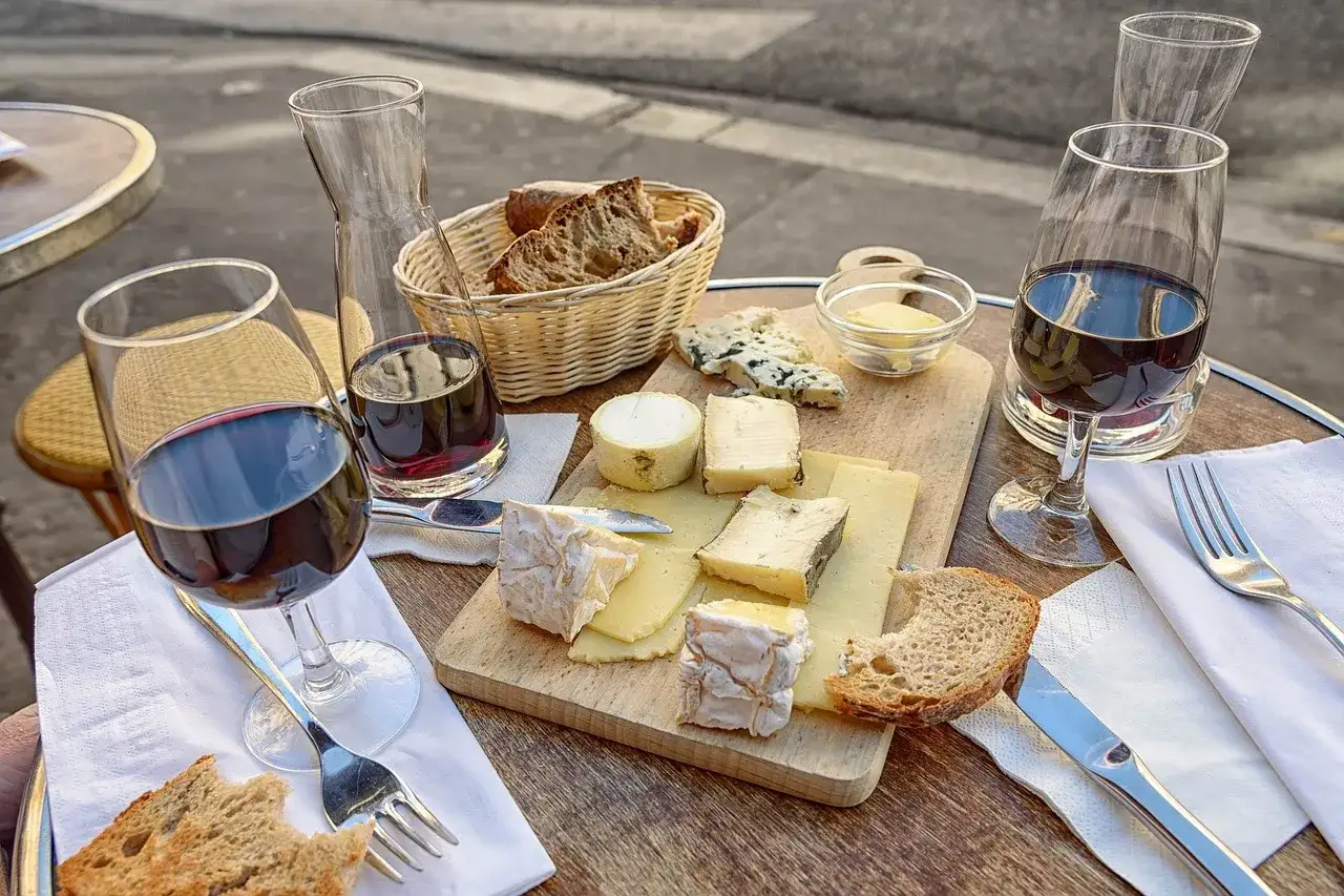 Tabla de quesos variados, pan rústico y copas de vino tinto, perfecta para una degustación.