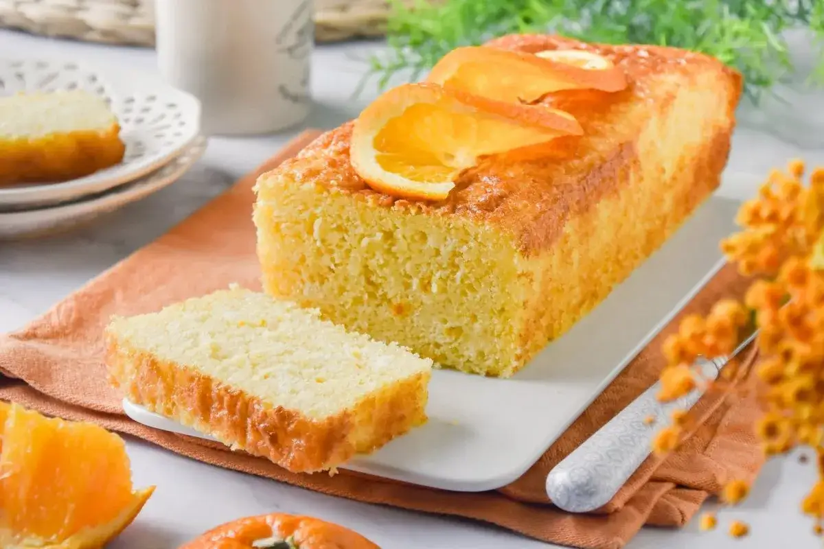 Tarta de naranja esponjosa, decorada con rodajas de naranja fresca. Un trozo ya cortado invita a disfrutar de su aroma cítrico.