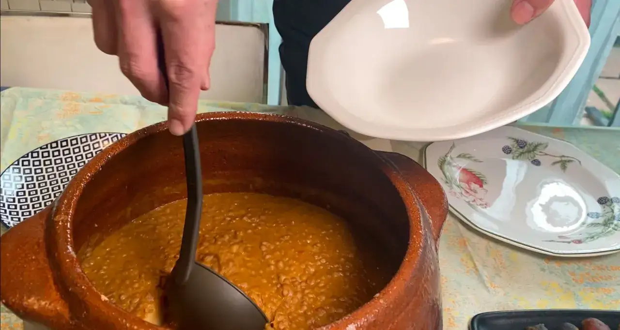 Sirviendo una deliciosa receta de lentejas de una olla de barro a un plato.