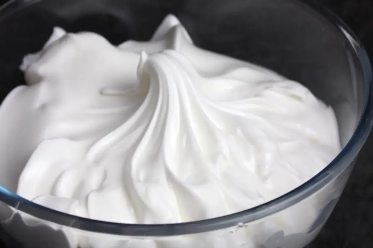 Merengue italiano sedoso y brillante en un bol de cristal, listo para decorar postres.