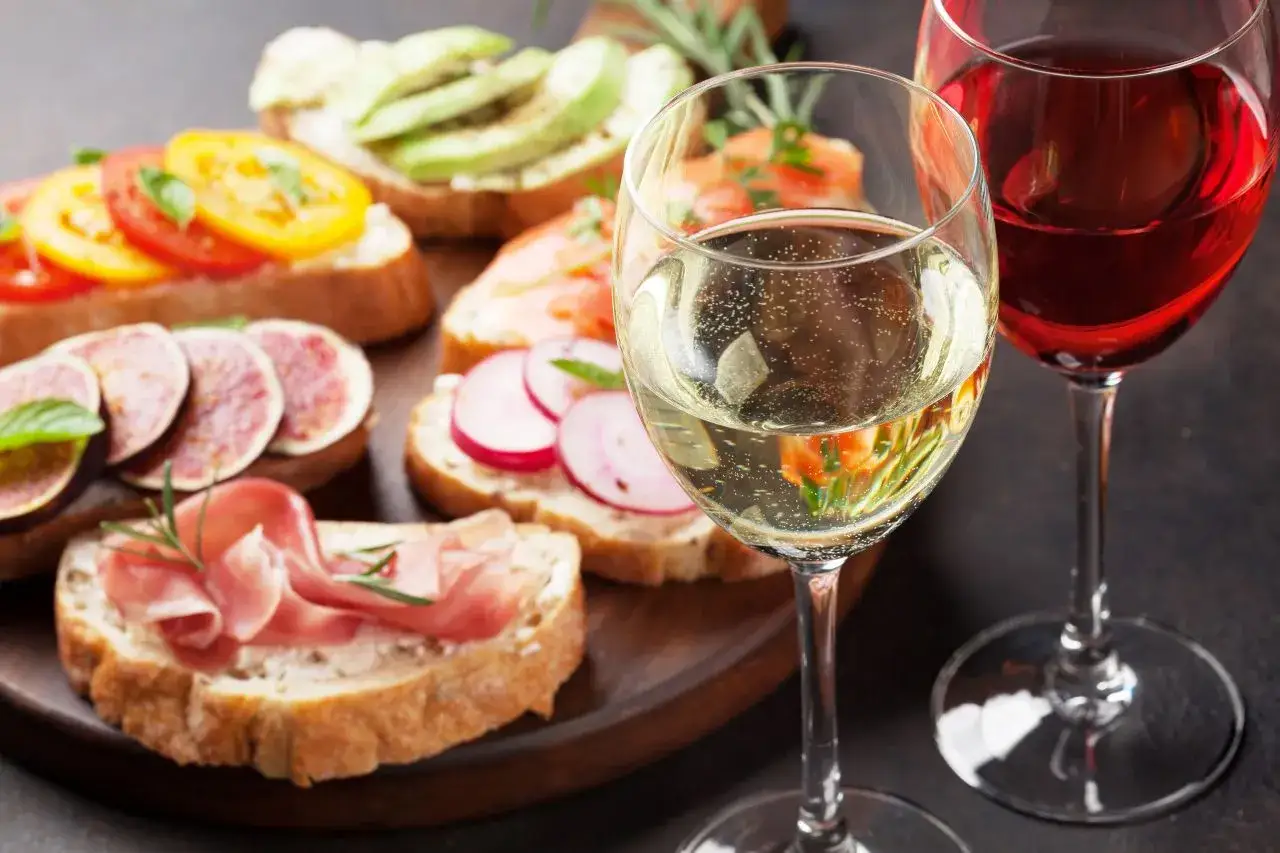 Brindis con vino seco y copas de vino blanco y tinto. Variedad de tapas con jamón, higos, salmón, aguacate y tomate.