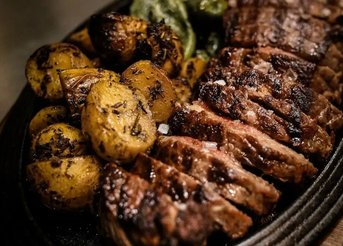 Ternera al horno jugosa, cortada en filetes, servida con patatas asadas doradas y hierbas aromáticas.