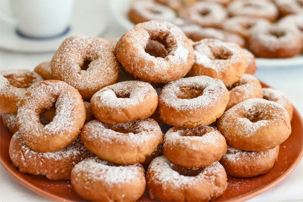Montón de rosquillas caseras esponjosas espolvoreadas con azúcar glas, listas para disfrutar con una taza de café.