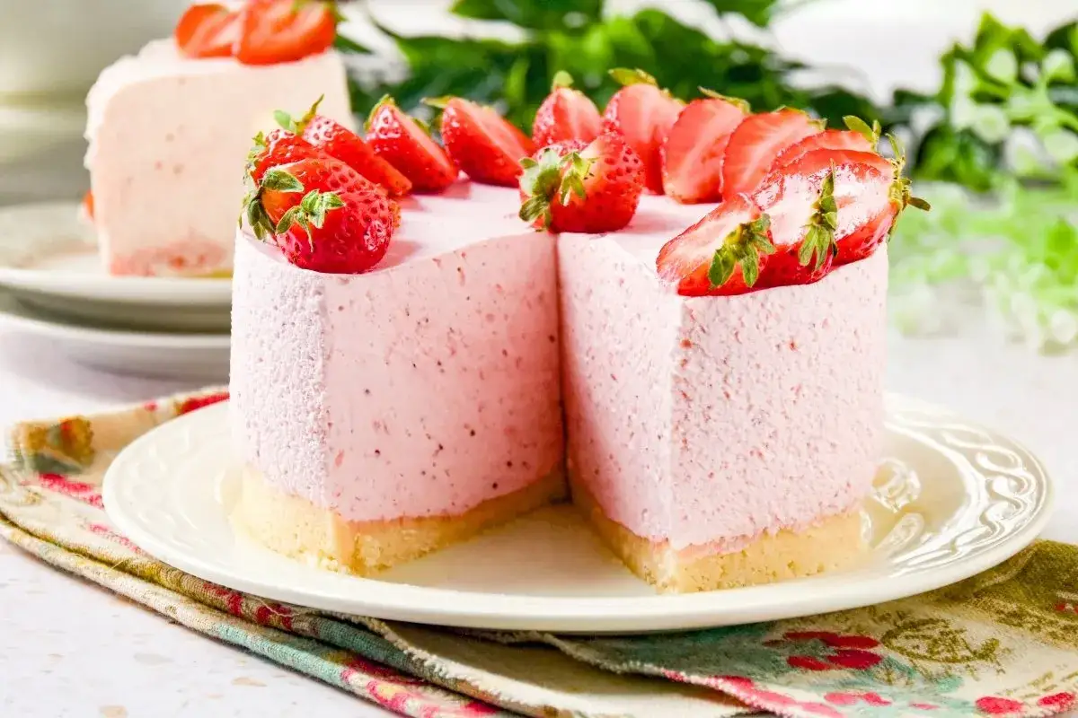 Deliciosa tarta de fresa, con una capa rosa cremosa y fresas frescas coronando la parte superior.