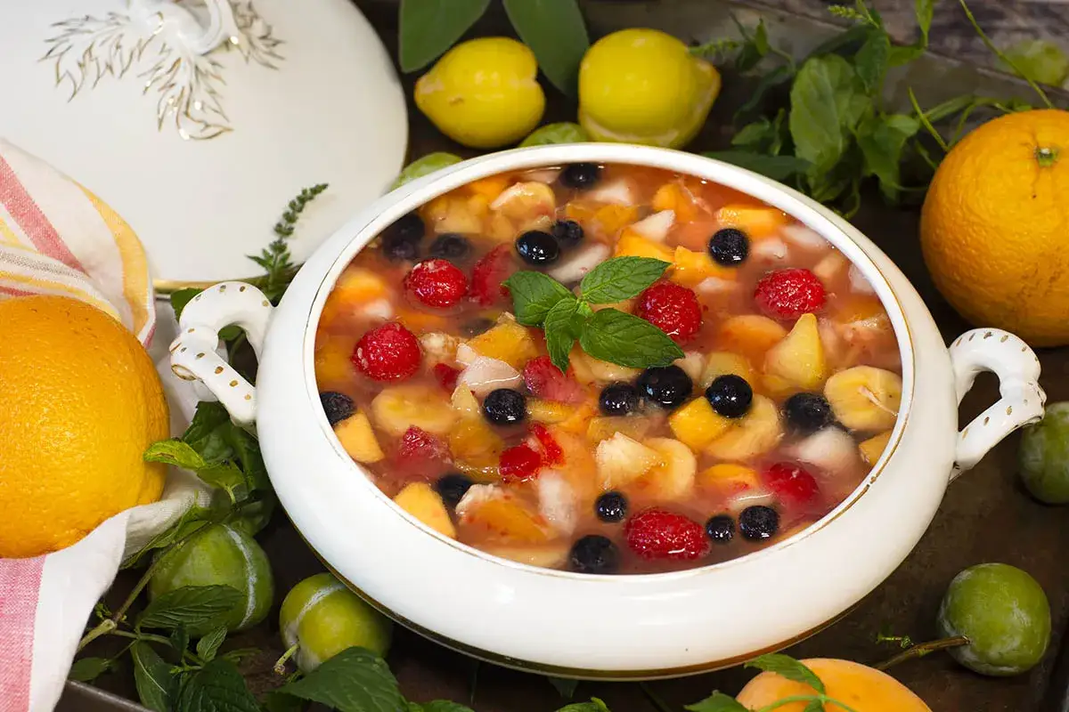 Un refrescante tazón de macedonia de frutas con fresas, arándanos, plátano y melocotón, adornado con menta.