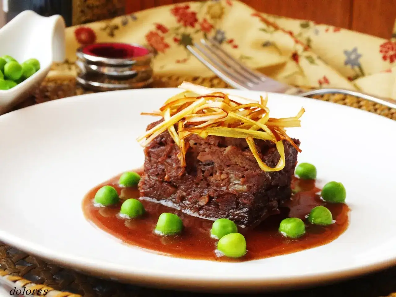Un trozo de falda de ternera estofada, servido con salsa y guisantes verdes.