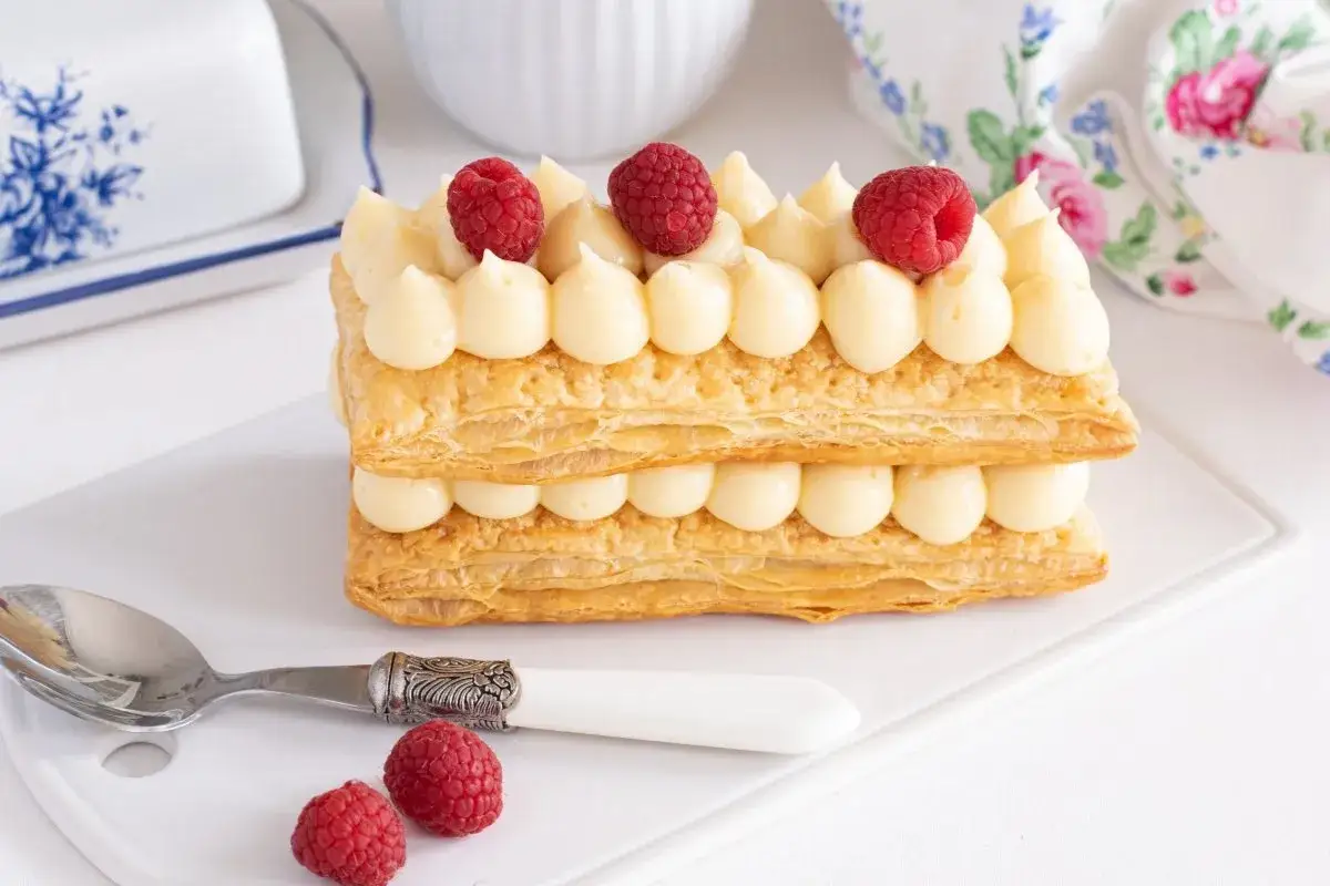 Delicioso pastel milhojas relleno de crema pastelera y decorado con frambuesas frescas.