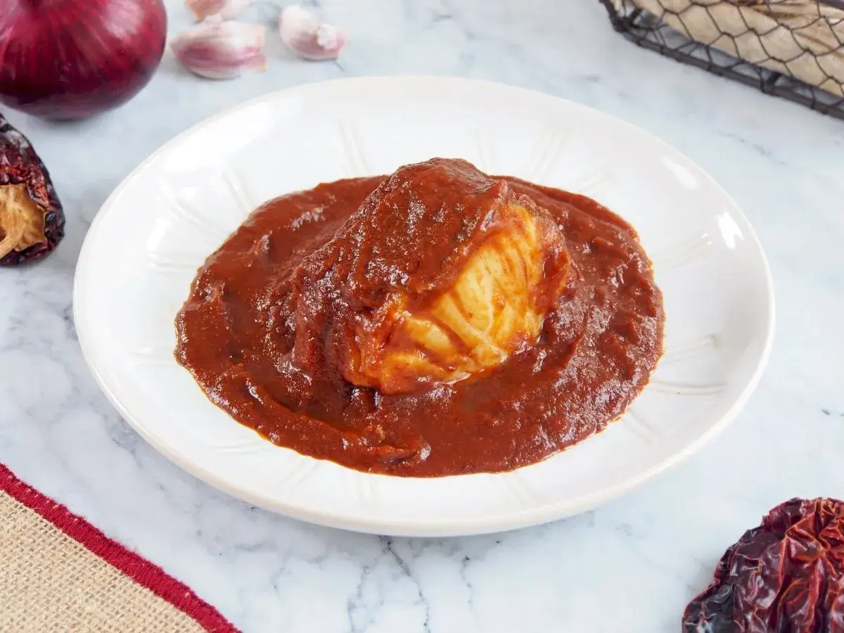 Un delicioso bacalao a la vizcaína, bañado en su salsa roja, con cebolla y ajos de fondo.