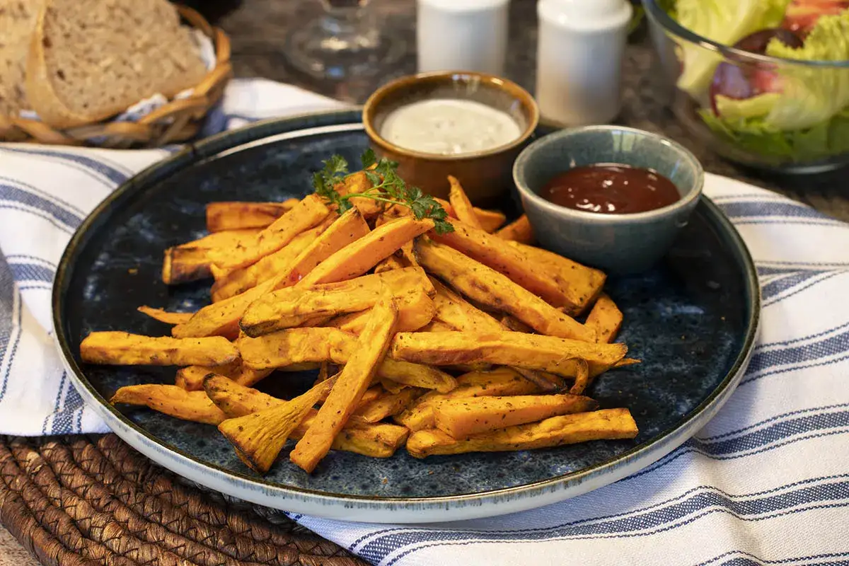 Boniato air fryer crujiente servido en plato azul con salsas y perejil.