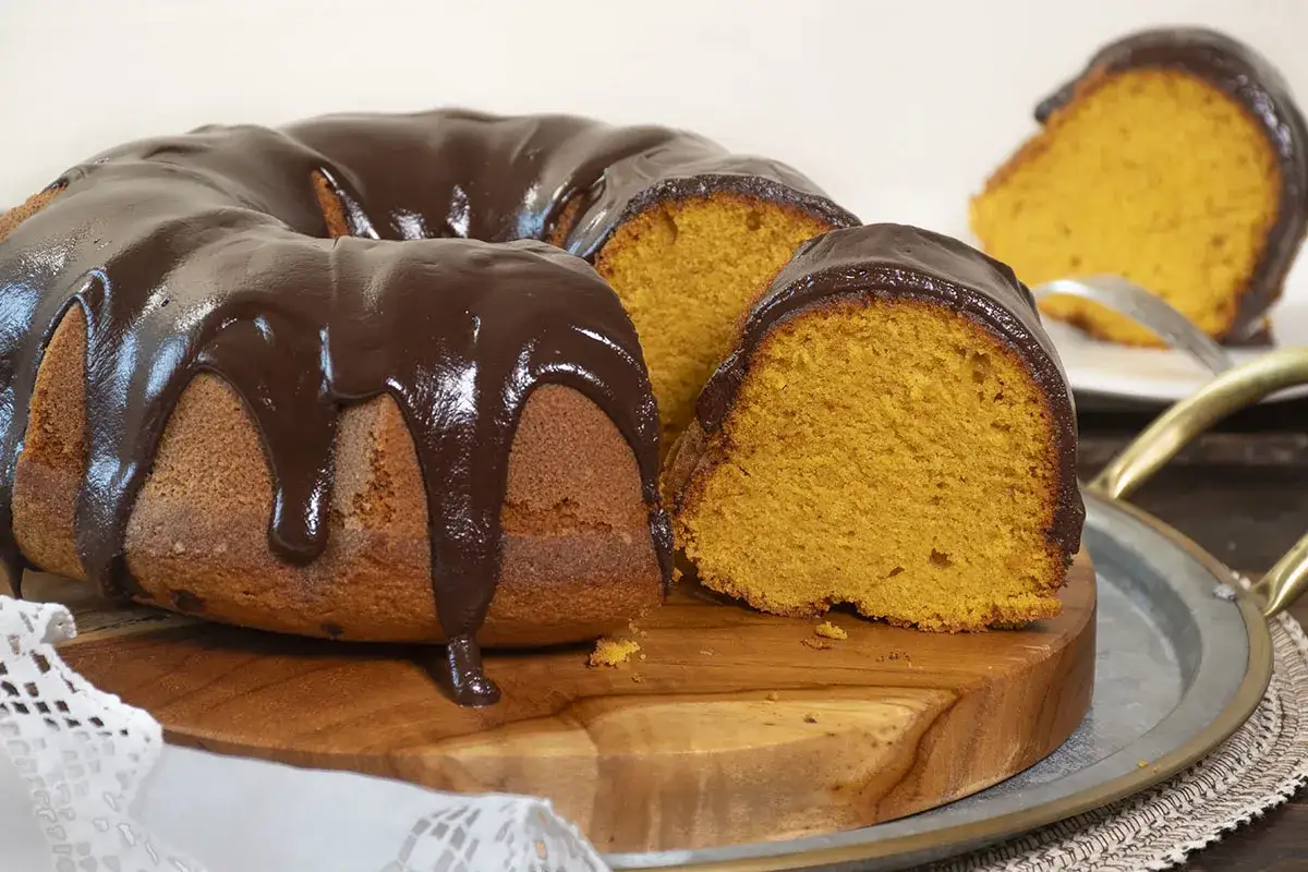 Bizcocho de calabaza cubierto con glaseado de chocolate, con una rebanada cortada para mostrar su interior esponjoso y naranja.