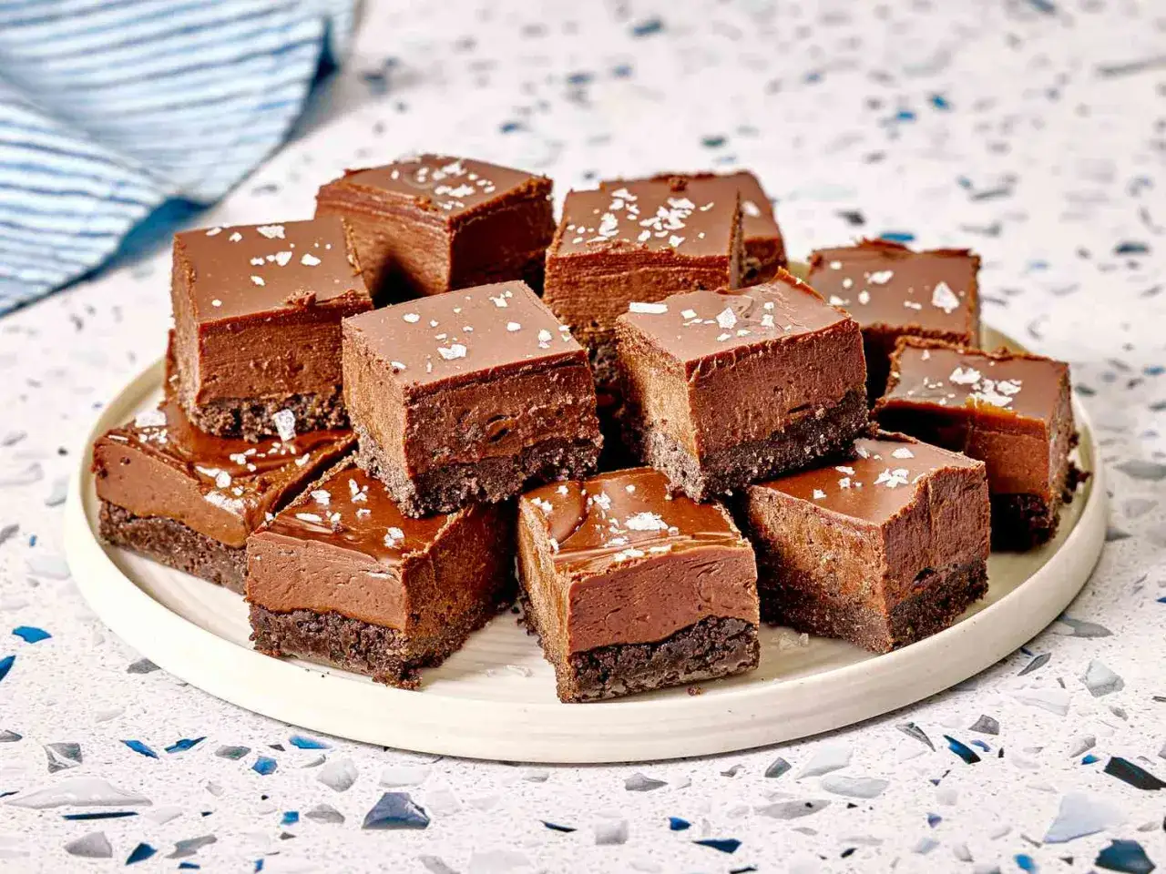 Deliciosa tarta de tres chocolates en cubos, con una base crujiente y cobertura brillante, espolvoreada con sal marina.