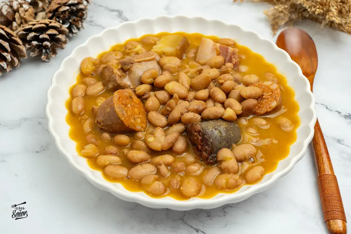 Un plato humeante de judías pintas con chorizo, morcilla y trozos de carne, listo para disfrutar.