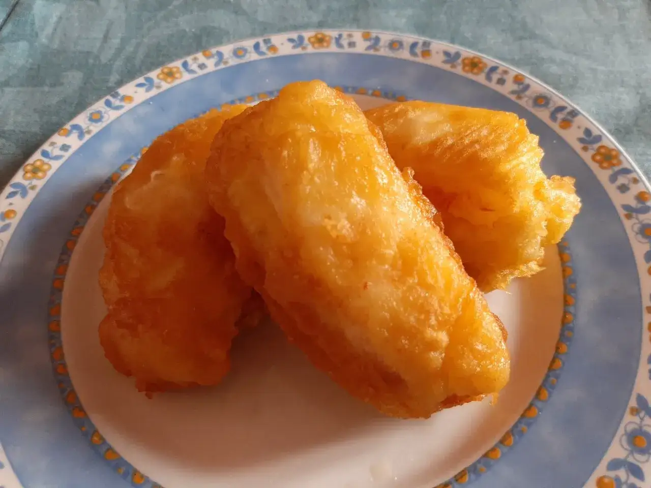 Tres trozos de bacalao rebozado dorados y crujientes en un plato con borde azul y flores.