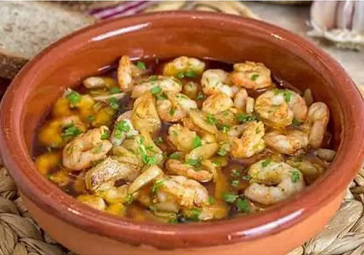 Gambas al ajillo burbujeantes en cazuela de barro, con pan rústico y ajo al fondo.