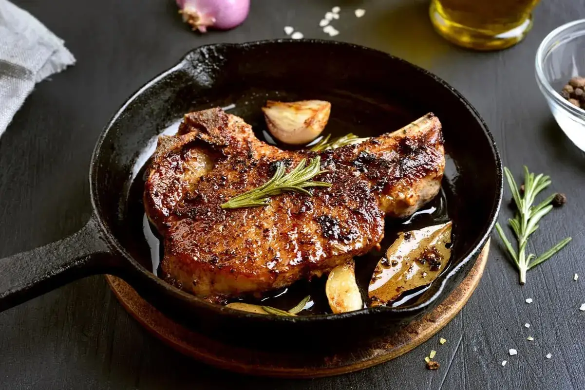 Chuleta de ternera al horno, jugosa y dorada, servida en sartén de hierro fundido con ajo, romero y laurel.