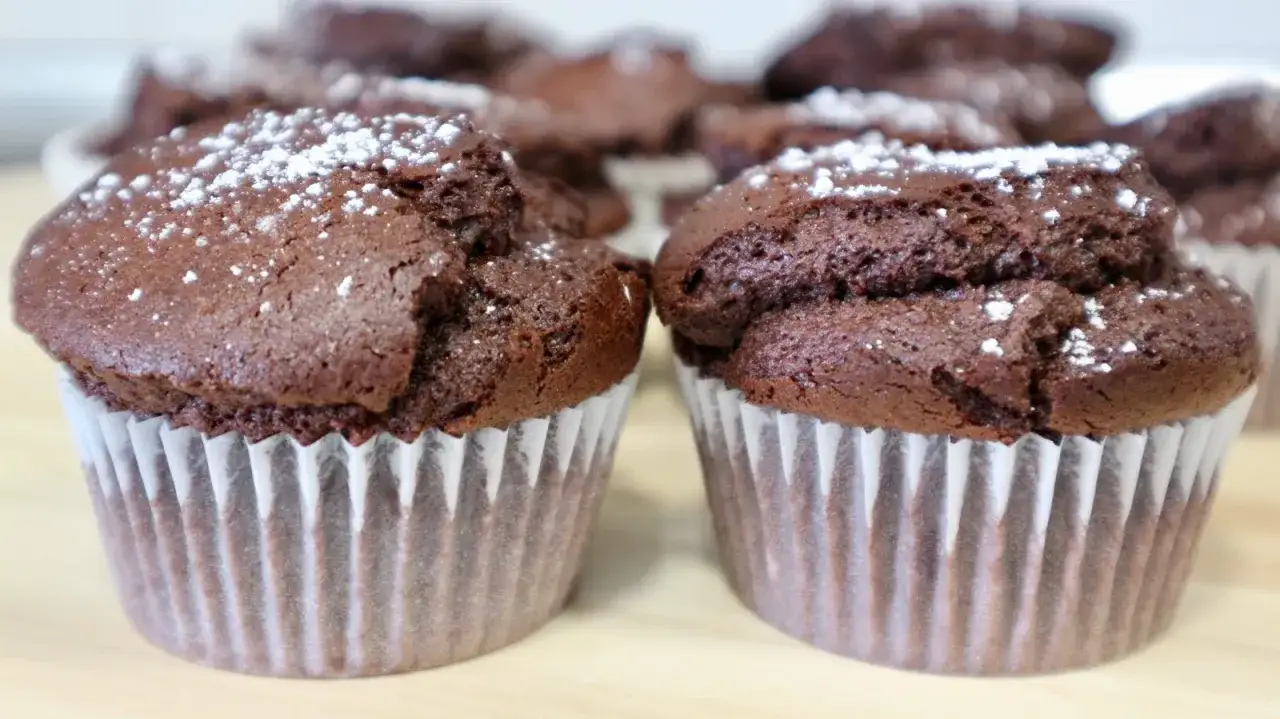 Dos magdalenas de chocolate recién horneadas, espolvoreadas con azúcar glas, listas para disfrutar.