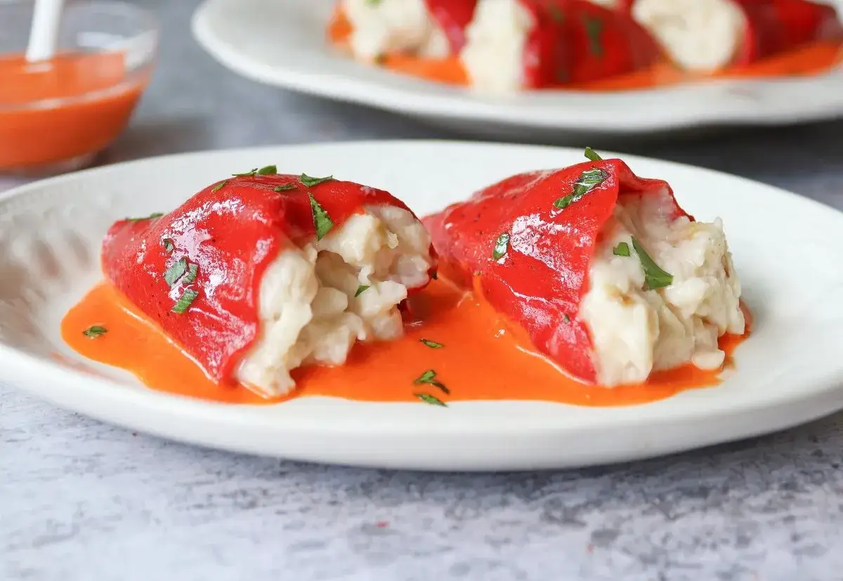 Dos pimientos rojos rellenos de arroz, cubiertos con perejil picado y servidos en una salsa naranja vibrante.