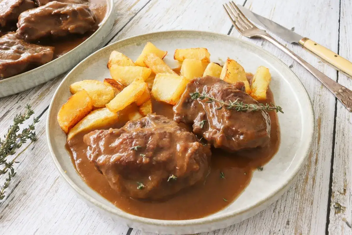 Dos tiernas patas de ternera guisada en su jugo, acompa&ntilde;adas de patatas r&uacute;sticas fritas y una ramita de tomillo fresco.