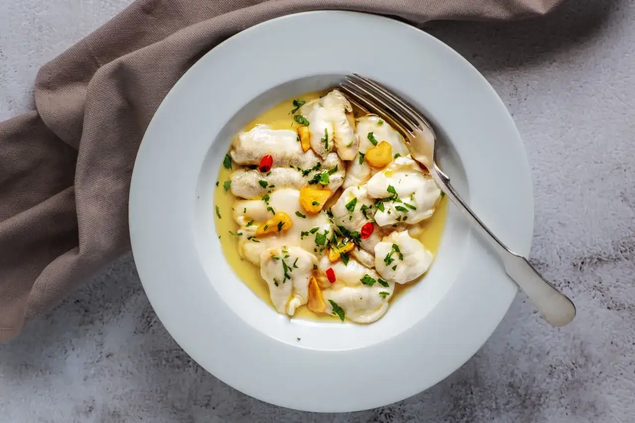 Bacalao al pil pil, un plato tradicional con trozos de pescado blanco en una salsa dorada, adornado con perejil, ajo y guindilla.