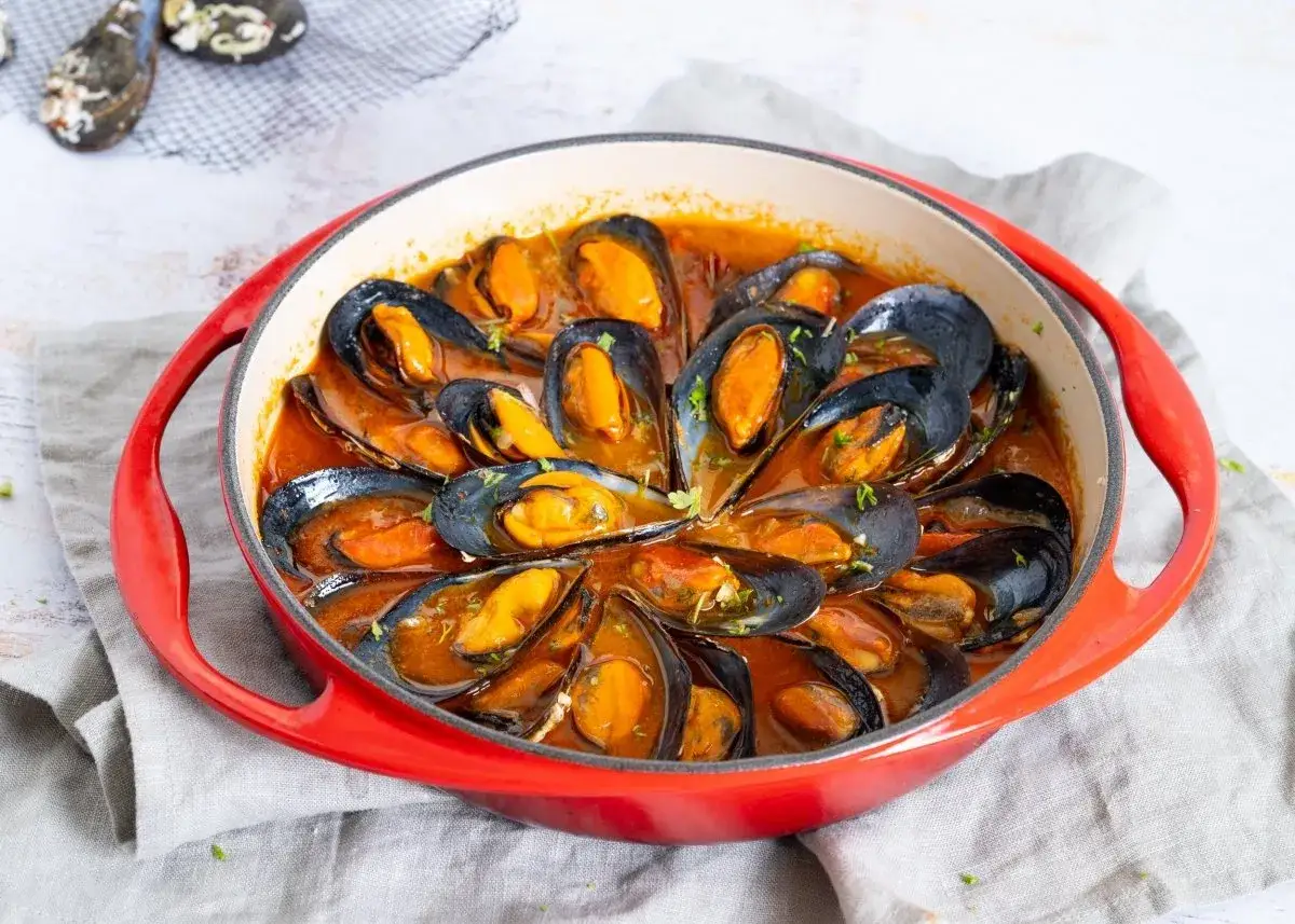 Mejillones a la marinera en cazuela roja, con salsa sabrosa y perejil picado. ¡Un plato delicioso!